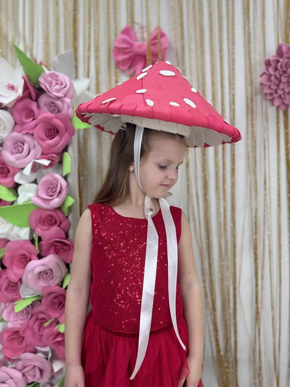 May include: A red mushroom hat with white spots, worn with a red sequined top and skirt. The hat has a white underside and is secured with white ribbons. The outfit is suitable for a costume or themed event.
