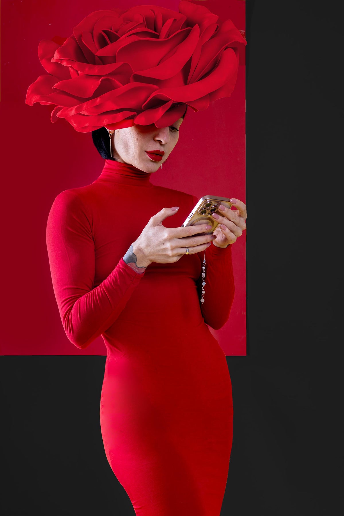 May include: A woman wearing a red dress and a large red rose hat is looking at a gold phone case with a pop socket.