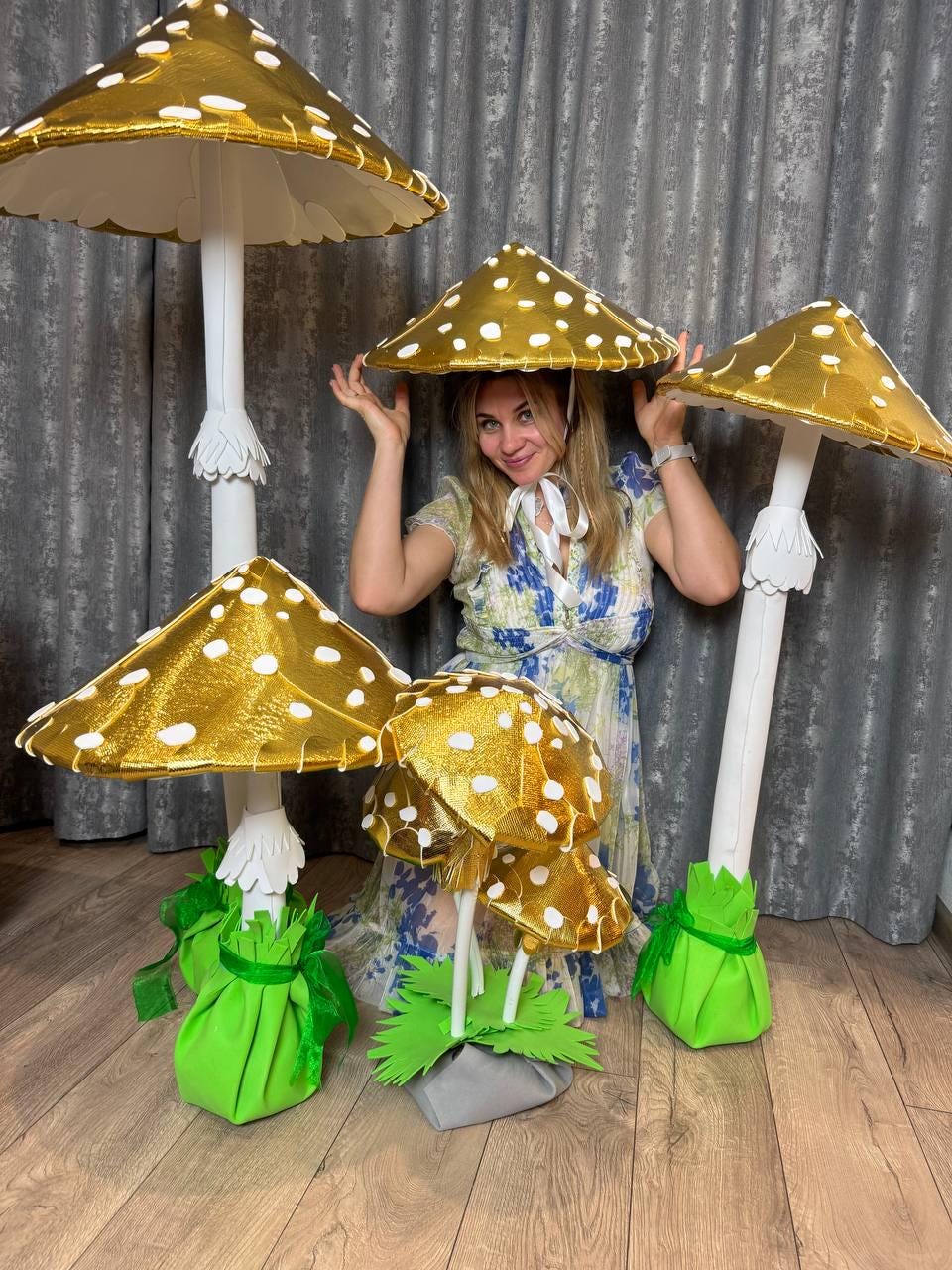 May include: Four large golden mushroom decorations with white polka dots. The mushrooms have green and white bases. A person is wearing a golden mushroom hat with white polka dots.