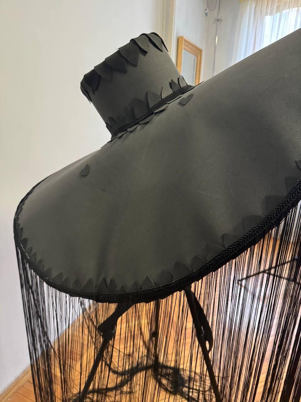 May include: A black wide-brimmed hat with a fringe trim. The hat is decorated with black felt leaves around the crown.