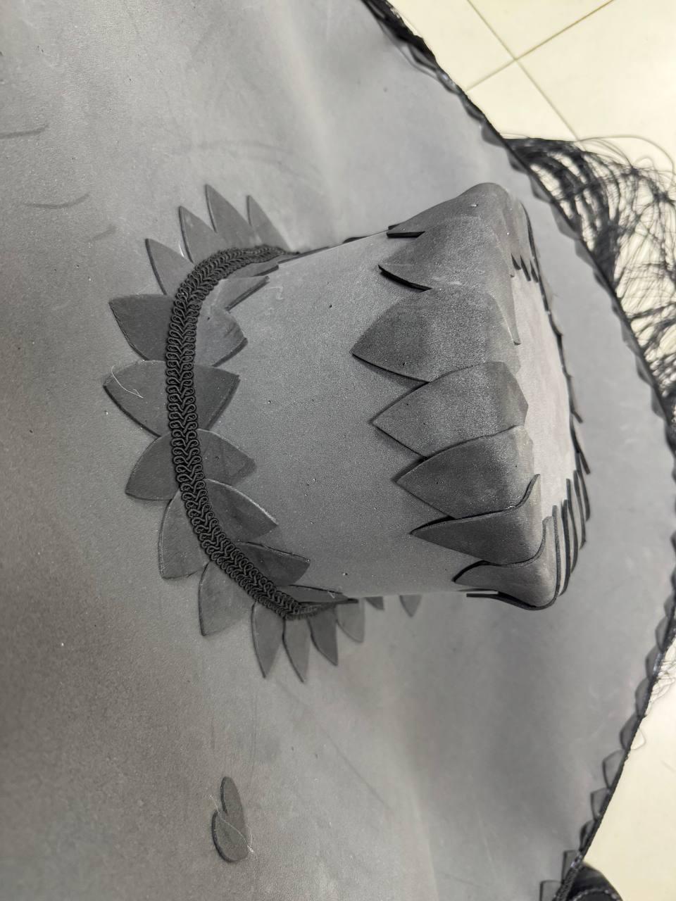 May include: A black sombrero with a wide brim and a decorative trim around the crown. The brim is scalloped and the crown is adorned with a row of black, pointed shapes.