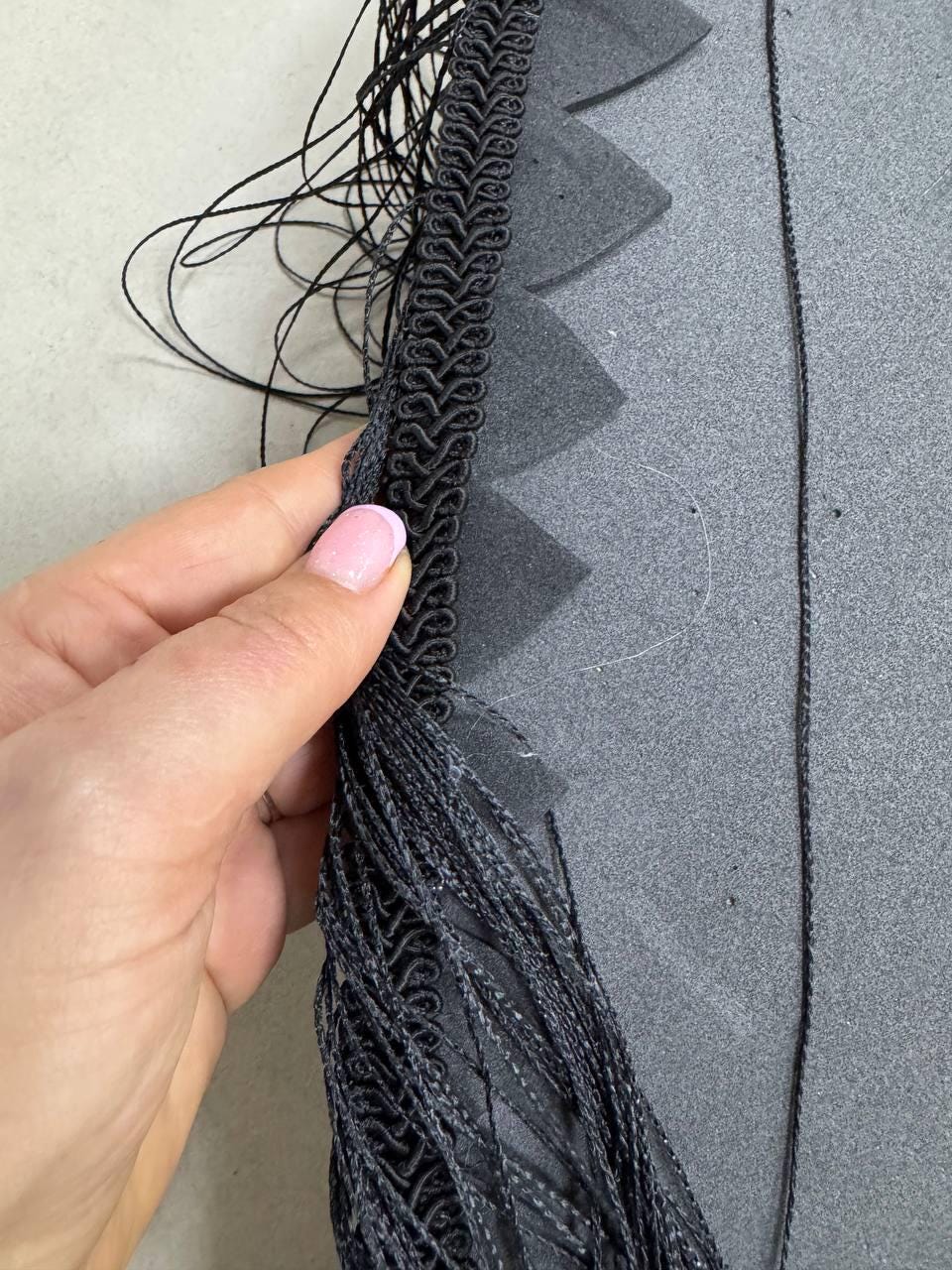 May include: Black fringe trim with a black braided cord sewn to a black fabric. The fringe is long and flowing.