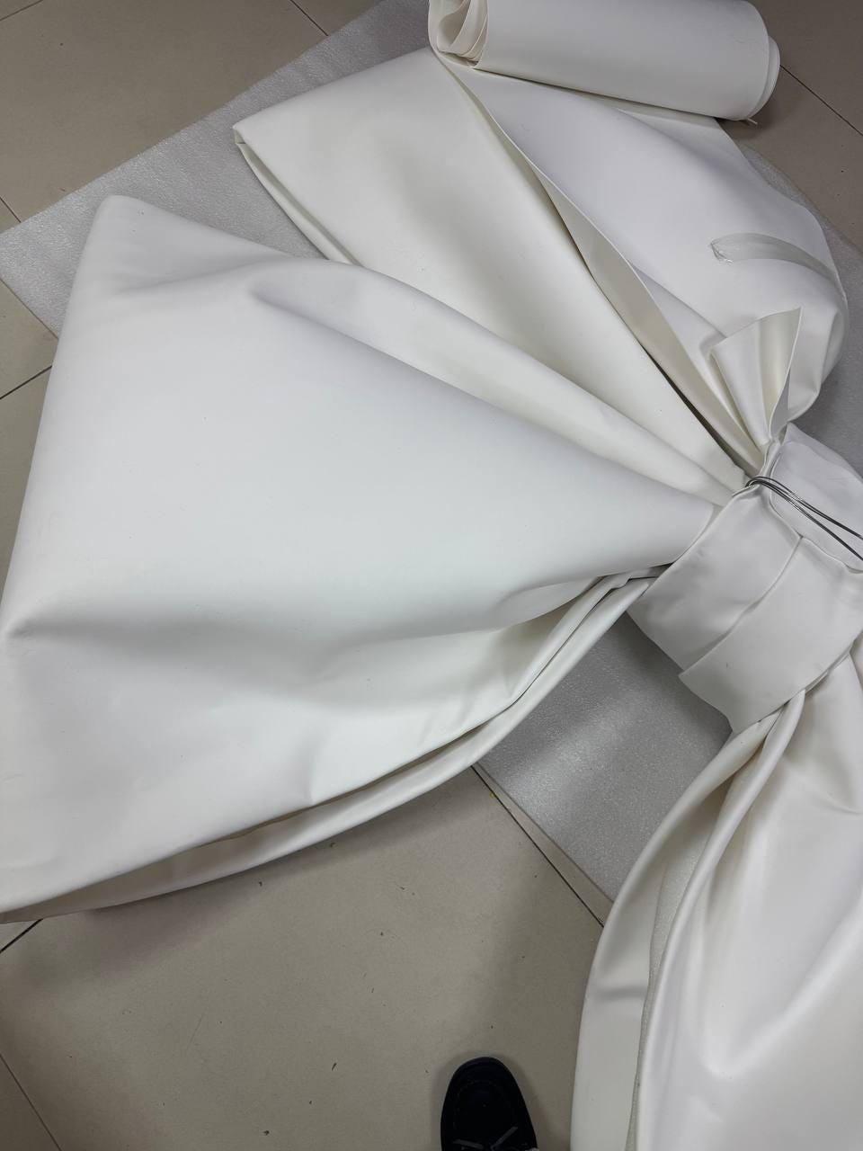 May include: A large white satin bow with a center loop and a long tail. The bow is folded and appears to be made of fabric.