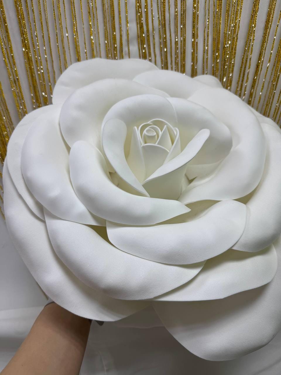 May include: A large, white, artificial rose with multiple layers of soft petals. The flower is in full bloom, with a detailed center and a smooth, matte finish. The rose is a decorative item, possibly for events or home decor.