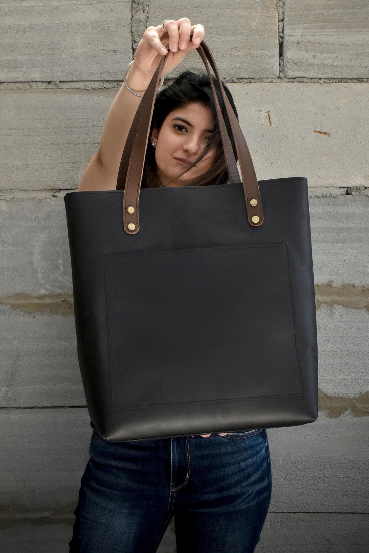 May include: A black leather tote bag with brown leather handles and a front pocket. The bag has gold-colored metal accents.