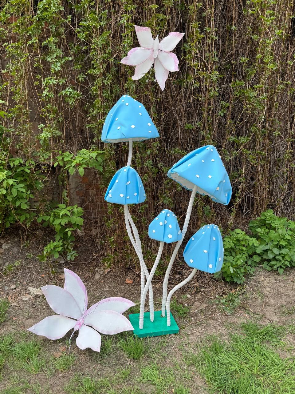 May include: A set of five blue and white mushroom-shaped decorations with white stems. The mushrooms are arranged in a cluster on a green base. Two white butterflies are on the ground in front of the mushrooms.
