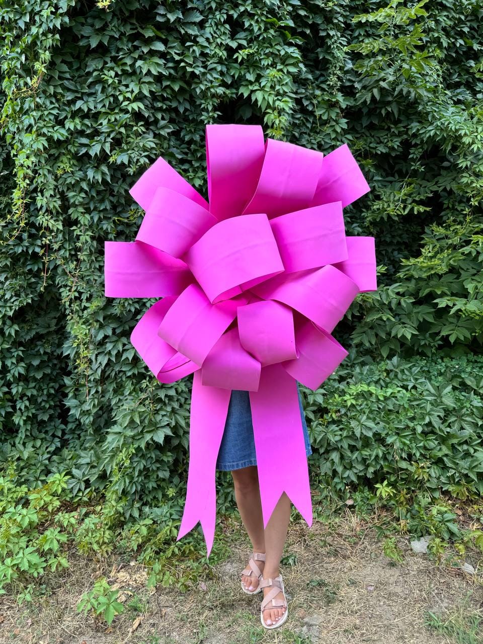 May include: A large, bright pink bow made of paper. The bow is large enough to cover a person's torso.