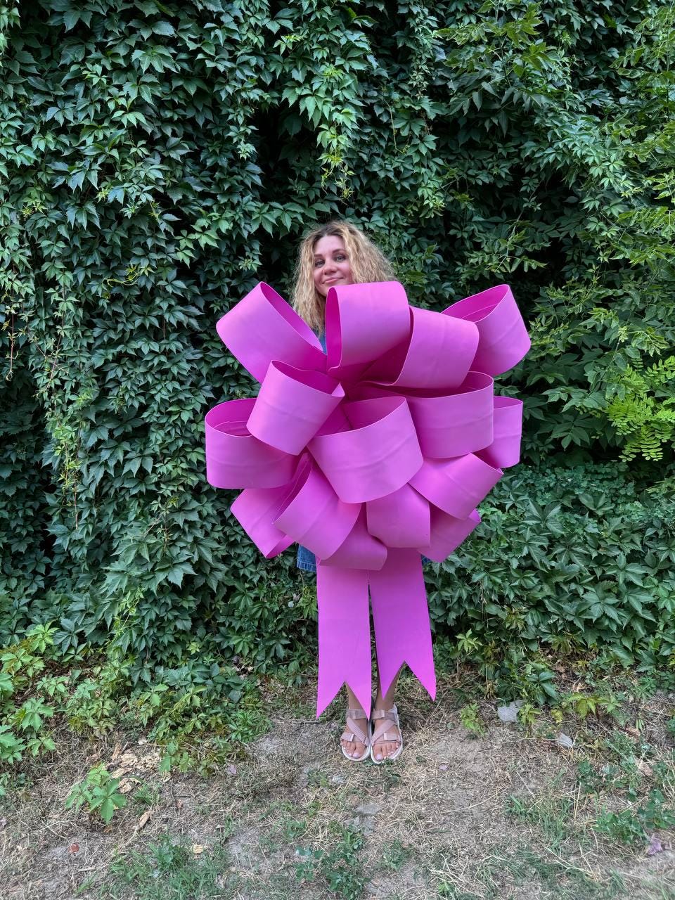 May include: A large pink bow with a long ribbon. The bow is made of multiple layers of fabric and is tied in a knot in the center. The ribbon is flowing down from the bow.