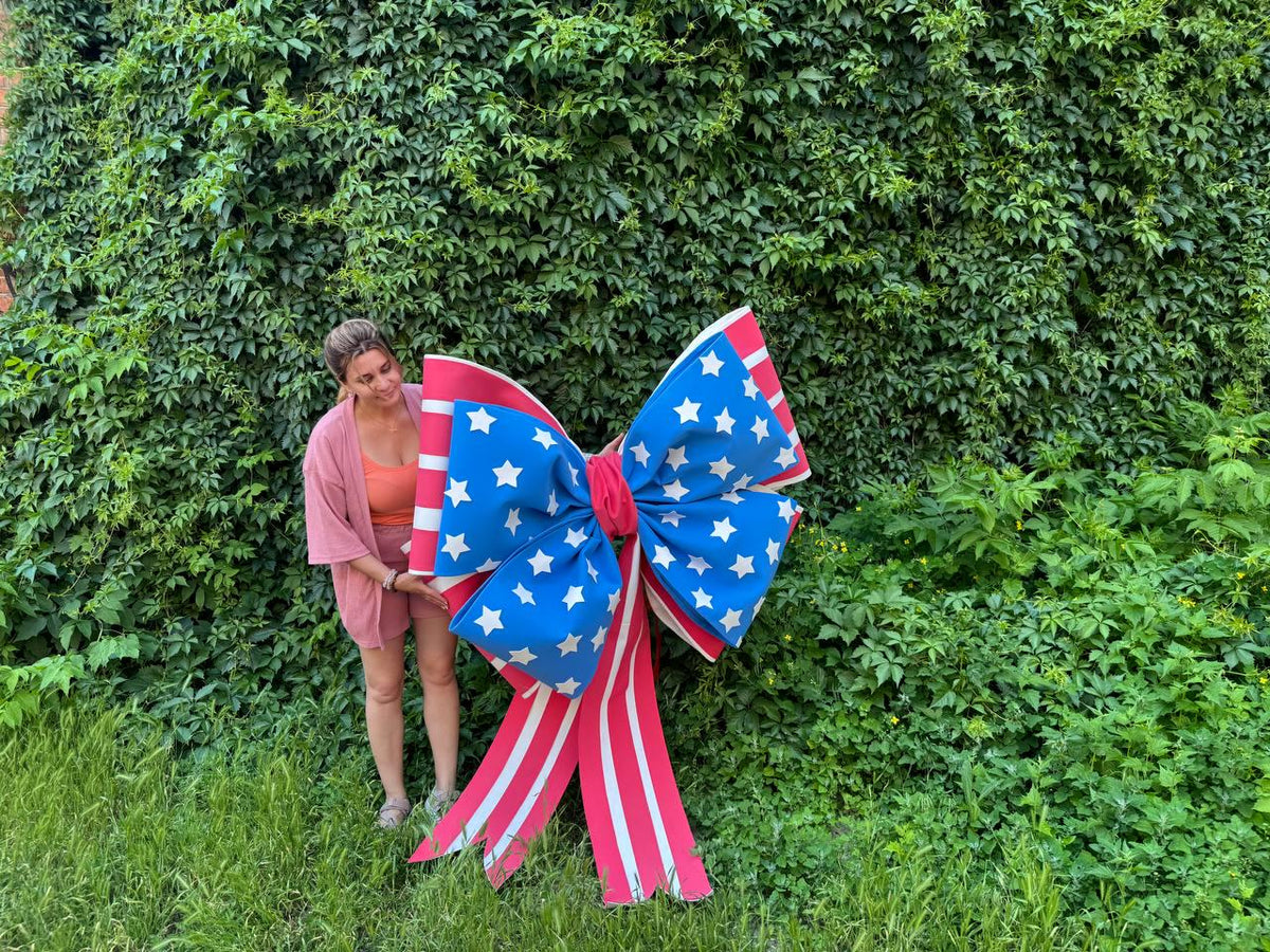 May include: A large decorative bow in red, white, and blue, featuring a star-studded blue center and red and white striped tails. The bow is designed to resemble the American flag, perfect for patriotic displays.