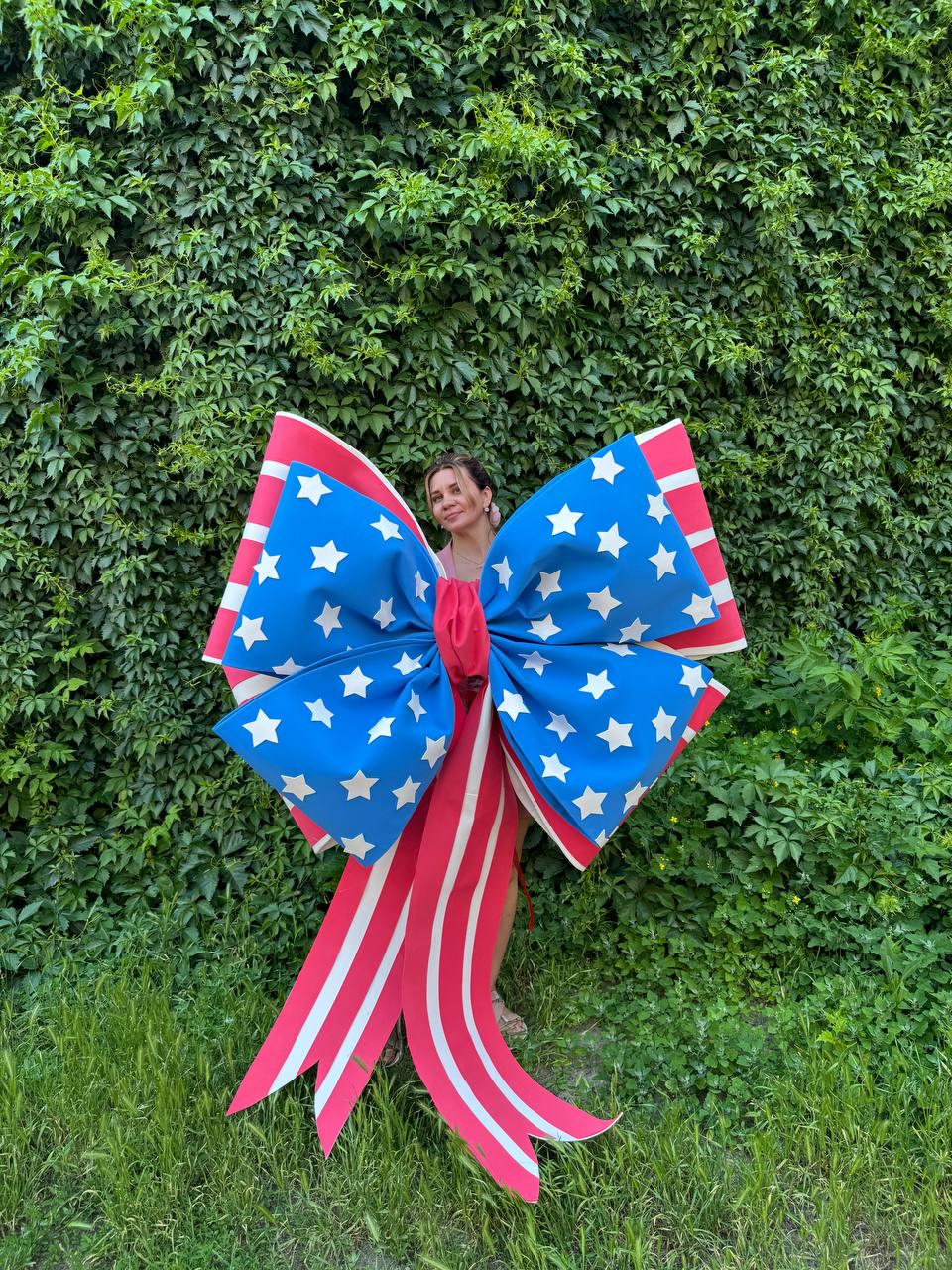 May include: A large decorative bow in red, white, and blue, featuring a patriotic design. The bow has a blue center with white stars and red and white striped ribbons. Perfect for Independence Day or other patriotic events.