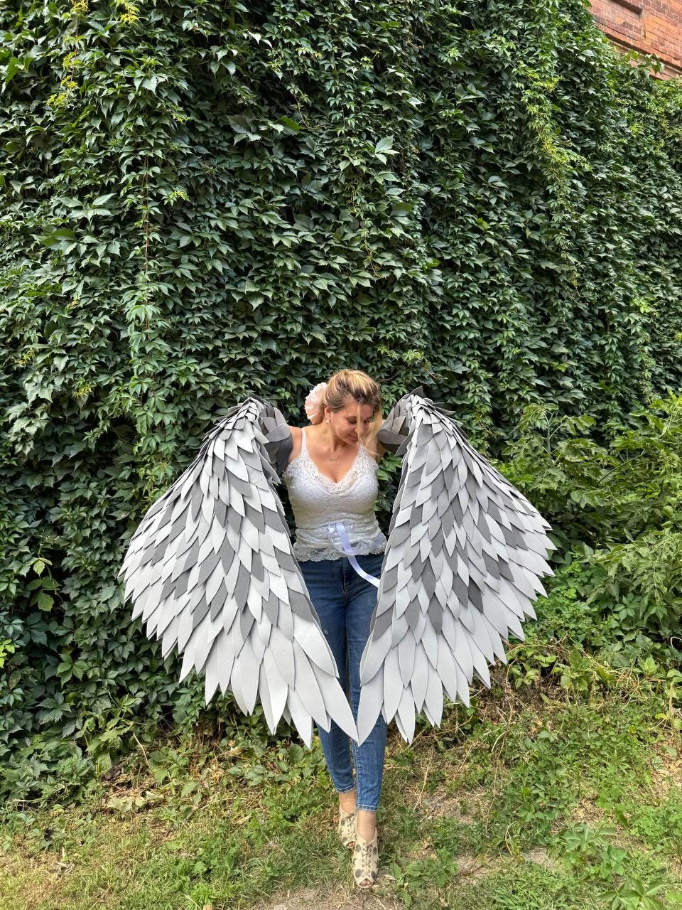 May include: Large, handmade angel wings with a layered feather design in shades of gray and white. The wings are spread wide, showcasing their intricate construction. The wings are a costume accessory.