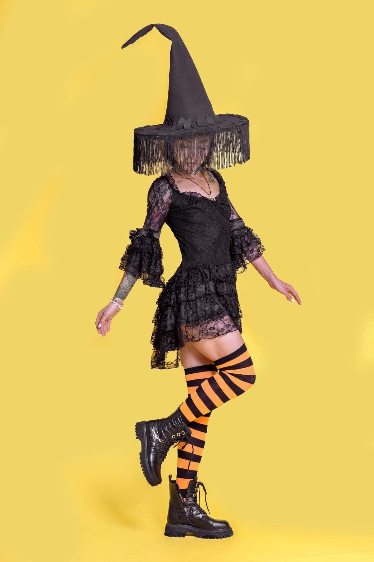 May include: A black witch costume with a tall, pointed hat, a lace dress, and striped orange and black thigh-high socks. The costume includes black combat boots, perfect for Halloween or costume parties.