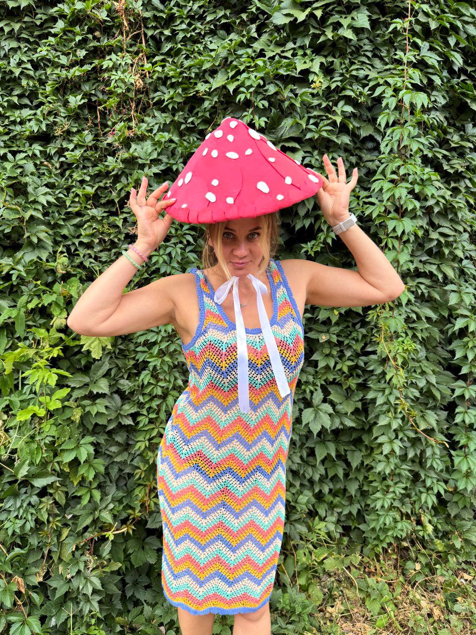 May include: A vibrant, handmade crochet dress with a colorful chevron pattern in shades of blue, orange, yellow, and purple. The dress is paired with a red mushroom-shaped hat with white spots. White ribbons are tied at the neckline.