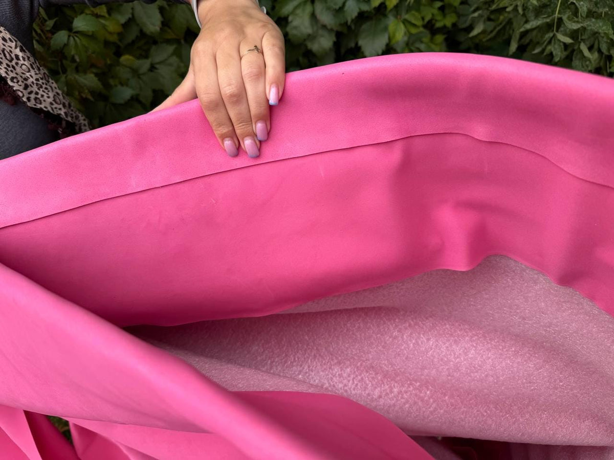 May include: Bright pink fabric, possibly leather or a similar material, is folded over to reveal a lighter pink, textured material underneath. The image is well-lit, showcasing the vibrant colors and textures of the materials.