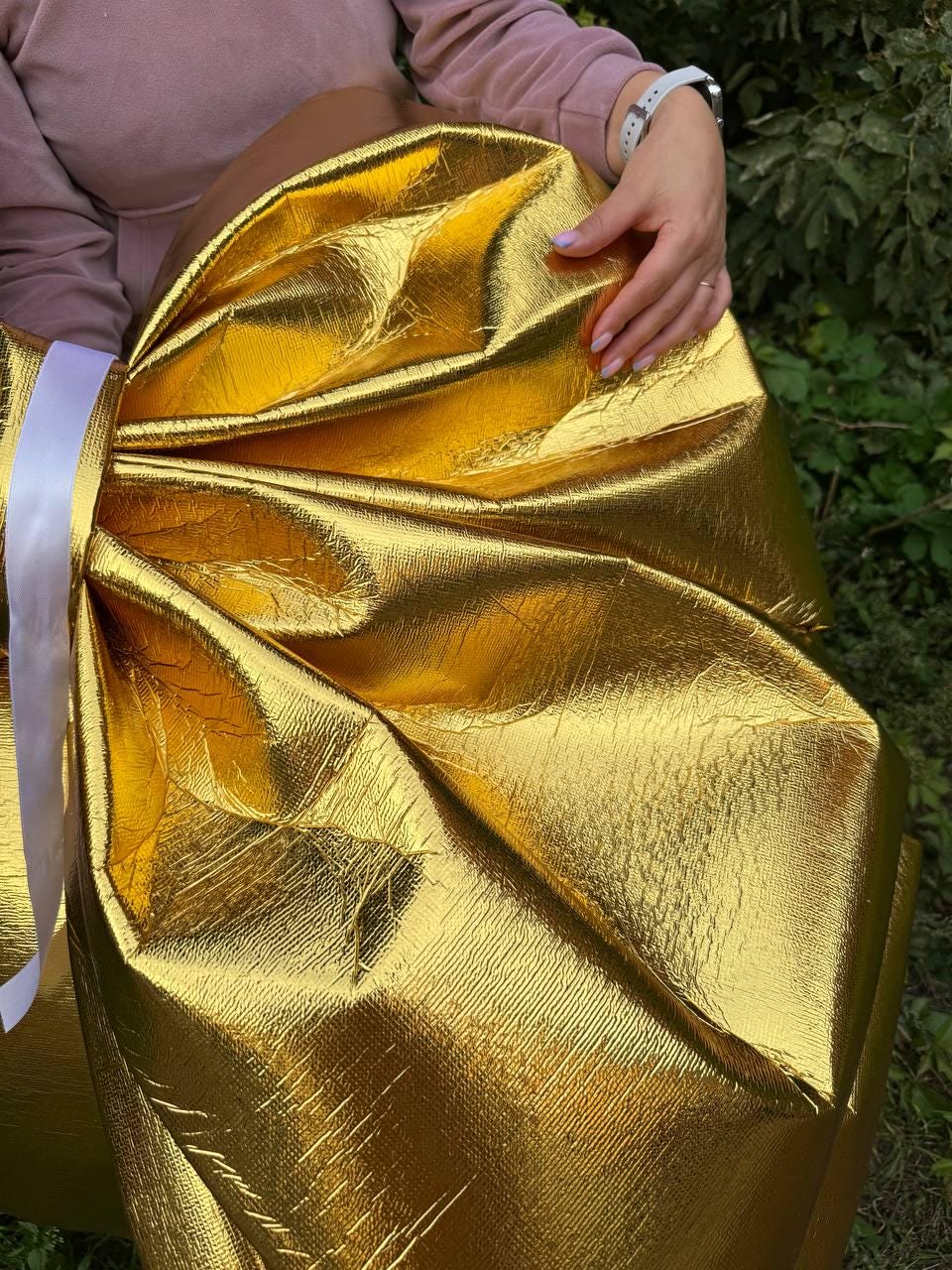 May include: A large, golden bow made of textured, metallic material. The bow is tied with a wide, white ribbon. The bow is a bright, shiny gold color and appears to be made of a durable material.