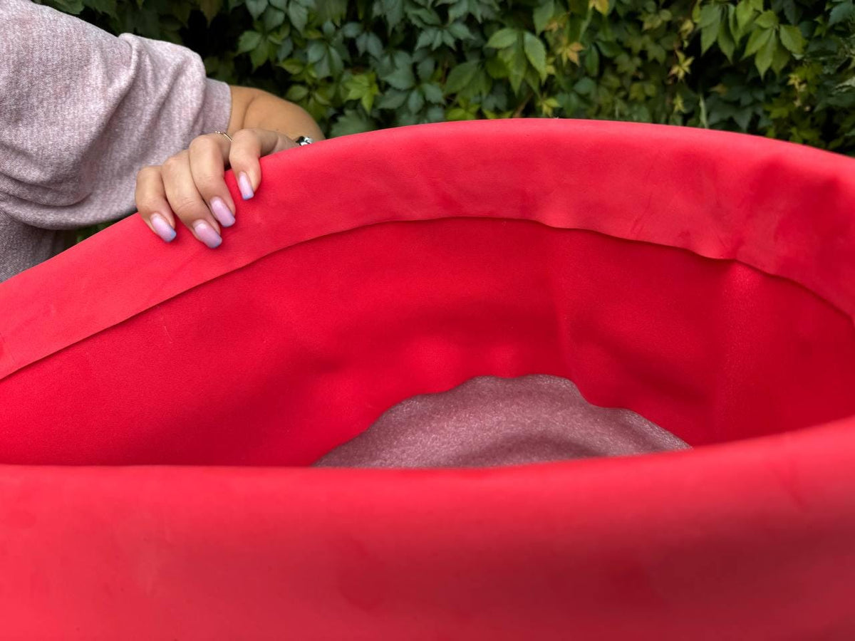 May include: A vibrant red, curved object, possibly a piece of fabric or a container, dominates the frame. The object's smooth surface contrasts with the texture of the background. The image is well-lit, highlighting the rich color and form.