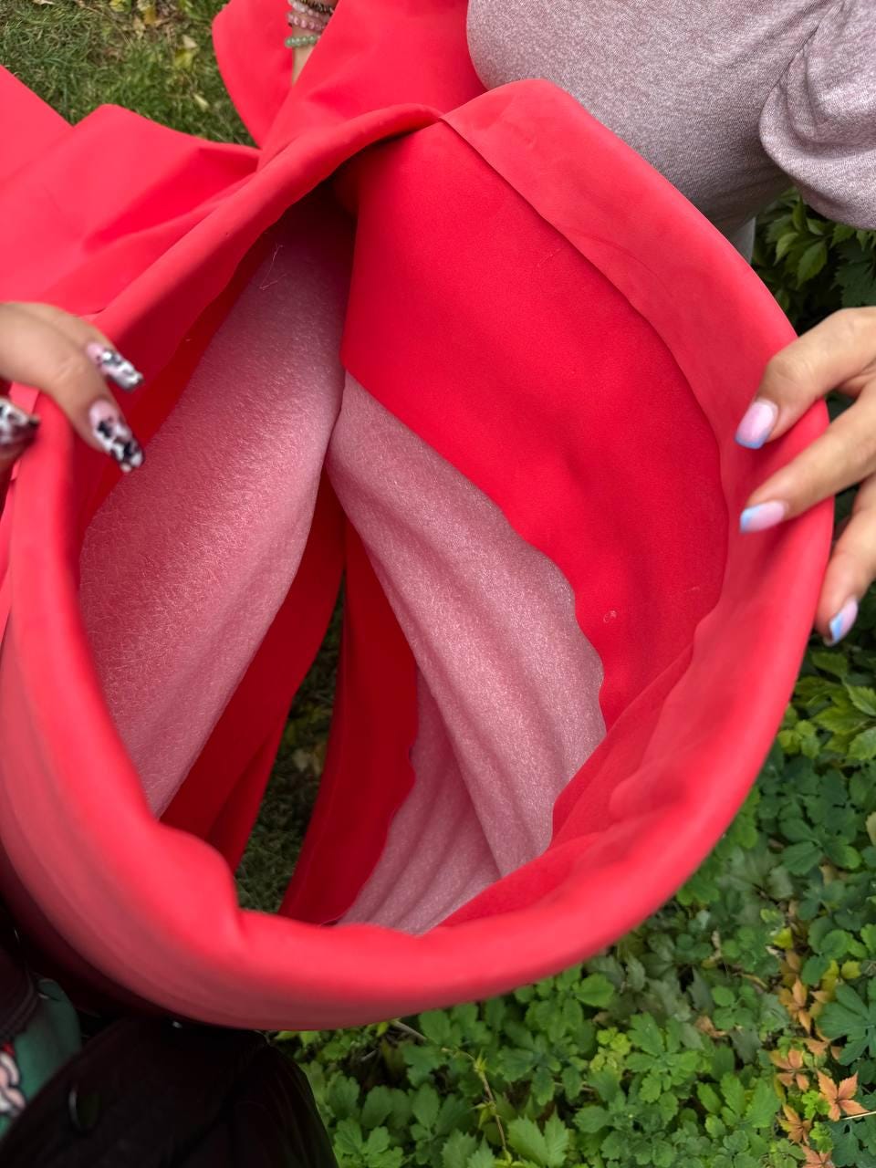 May include: A bright red cylindrical container with a smooth exterior and a soft, light pink foam lining visible inside. The structure is flexible and open at the top, revealing the contrast between the vibrant red outer layer and the pale interior.