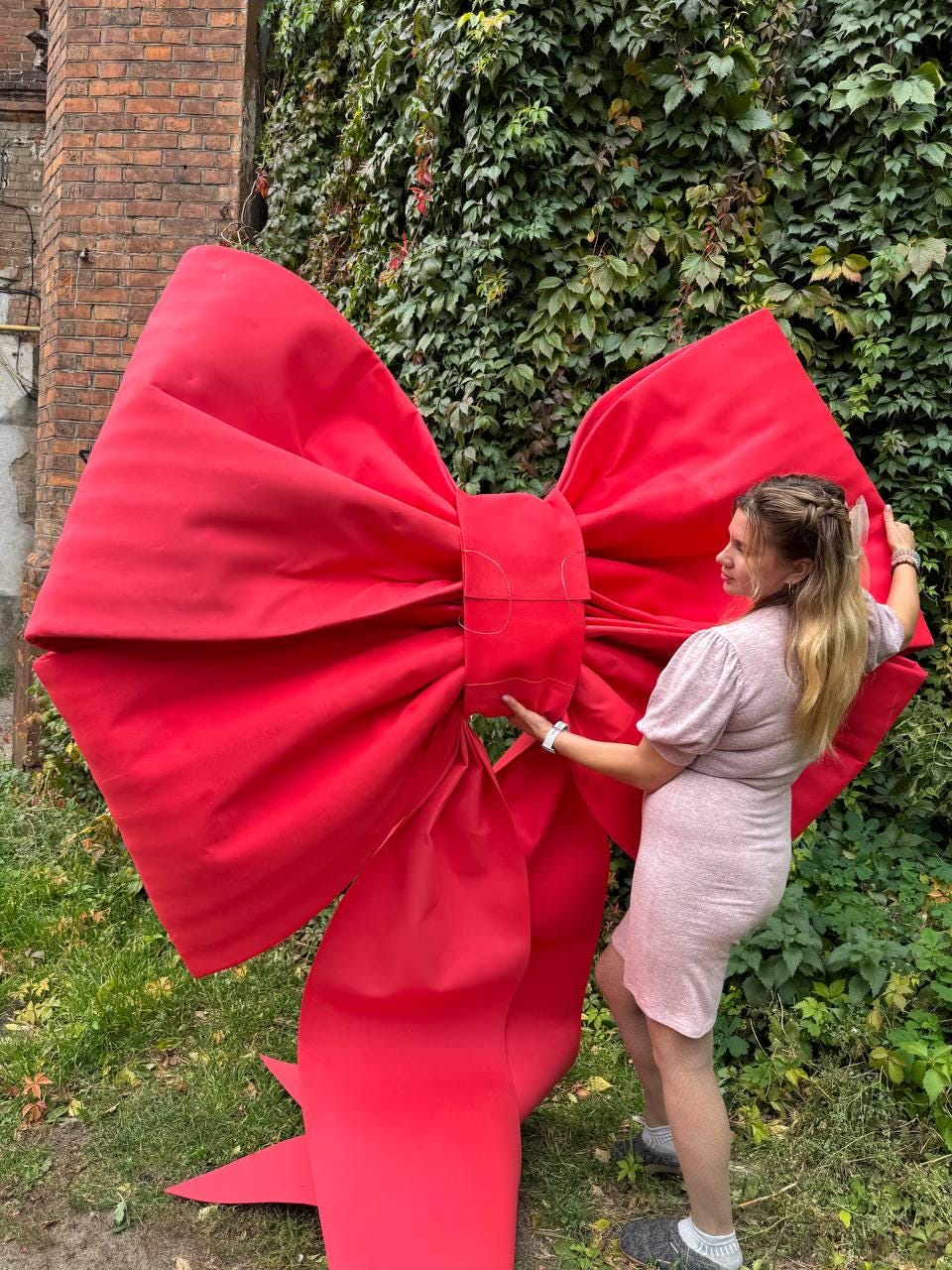 May include: A large, vibrant red bow, likely for decoration or a special event. The bow is made of a soft, possibly fabric material, and is held by a person. The bow's size suggests it could be used for a grand display or as a photo prop.