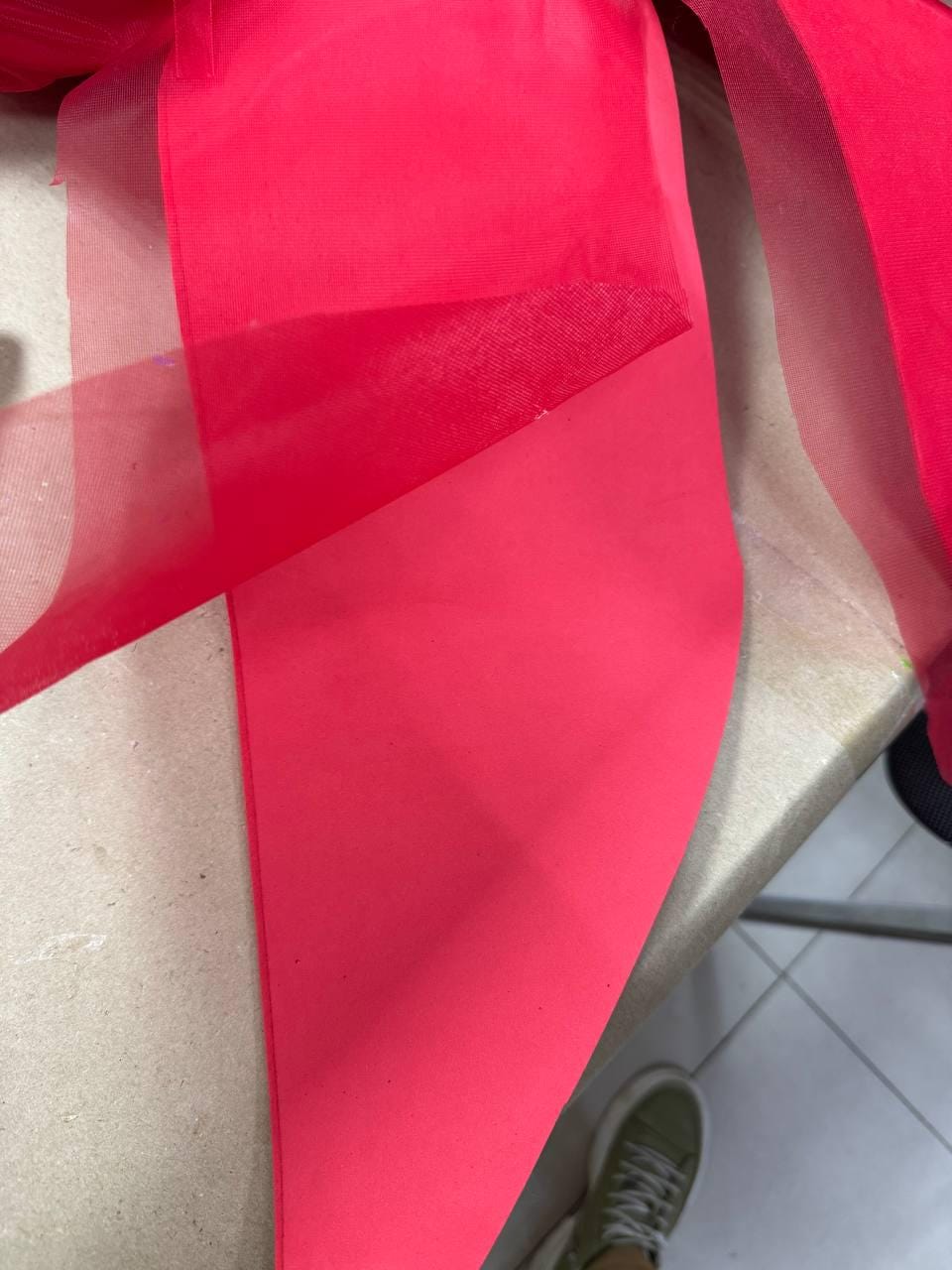 May include: Close-up of vibrant red fabric, possibly tulle or a similar sheer material, layered and folded. The fabric's texture is visible, with a slight sheen. The image suggests a craft or textile project, showcasing the material's color and drape.