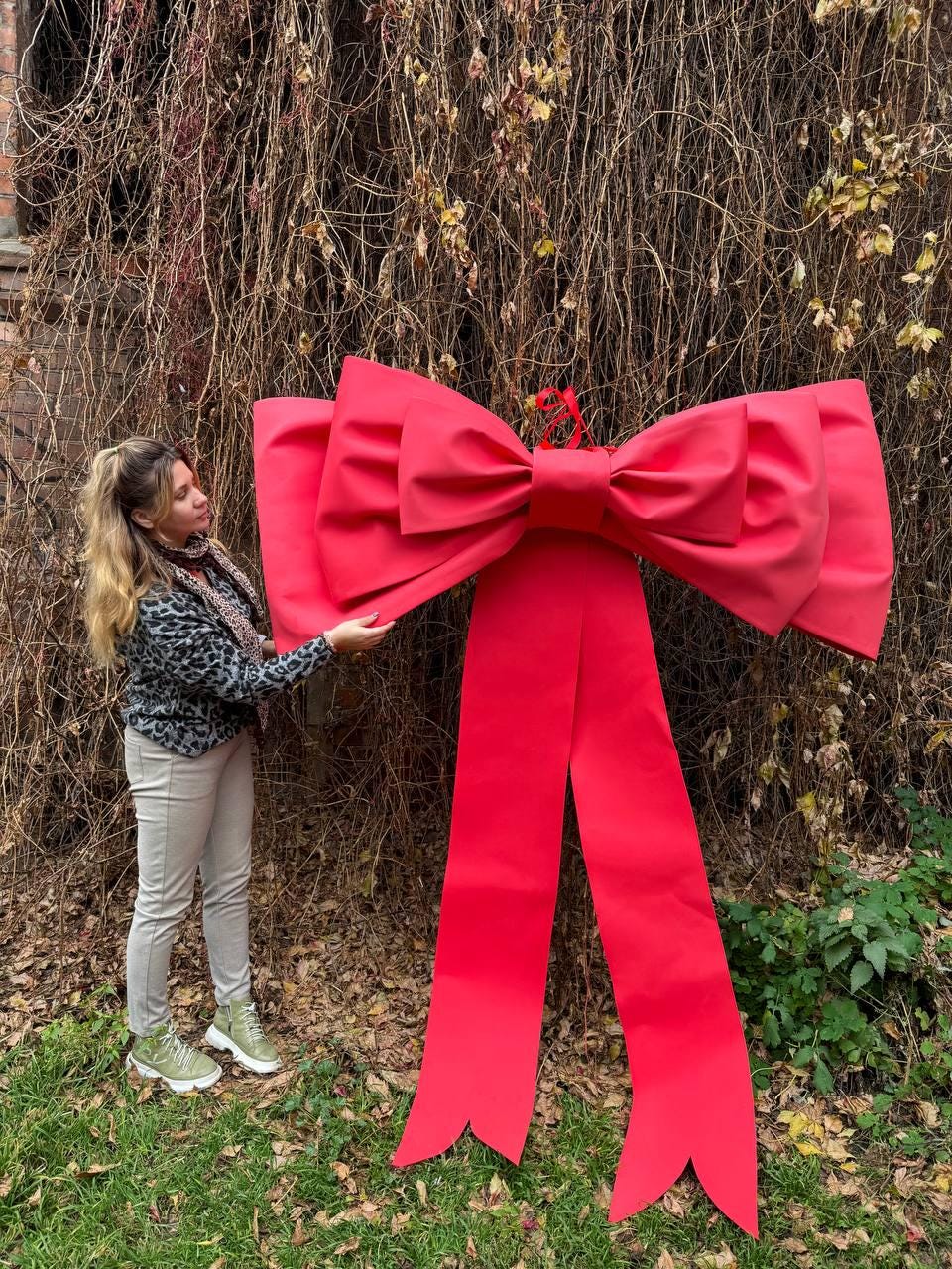 May include: A large, vibrant red bow with long, flowing ribbons. The bow is made of a smooth material and is designed for decorative purposes. The bow is large enough to be used as a festive decoration for a holiday or special event.