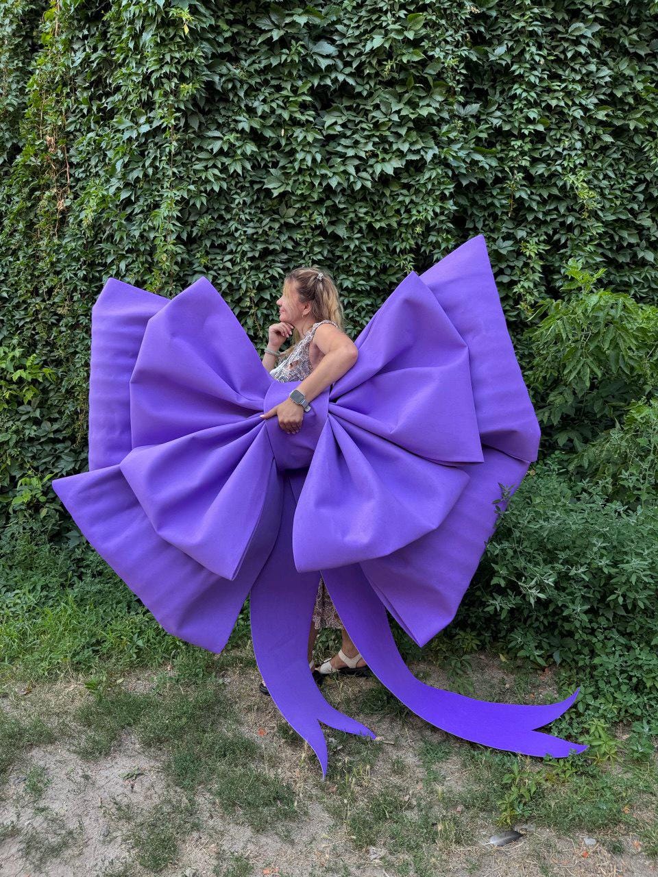 May include: A large, vibrant purple bow with long, flowing tails. The bow is made of a smooth, solid material and is the focal point of the image. The bow is large enough to be worn or used as a decorative element.