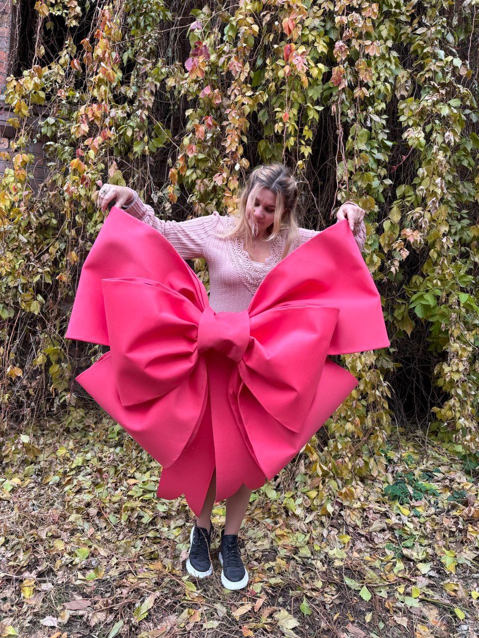 May include: A large, vibrant pink bow, held open against a backdrop of autumn foliage. The bow's size and color make it a striking visual element. The bow is the focal point, with its bold color and shape.
