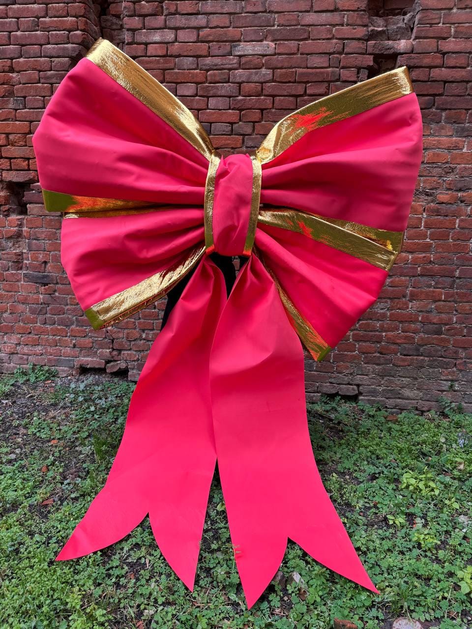 May include: A large, vibrant pink bow with gold trim. The bow is made of a shiny fabric and has long, flowing tails. The bow is likely for decoration, possibly for a gift or event.