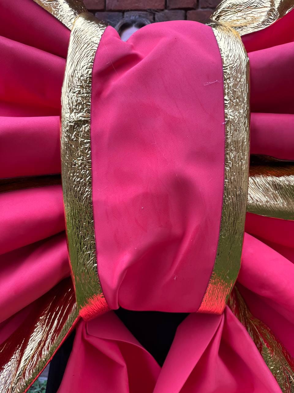 May include: A large, vibrant pink bow with gold trim. The bow is made of a soft, possibly fabric material, and is designed with multiple layers and folds. The gold trim adds a touch of elegance and contrast to the bright pink color.