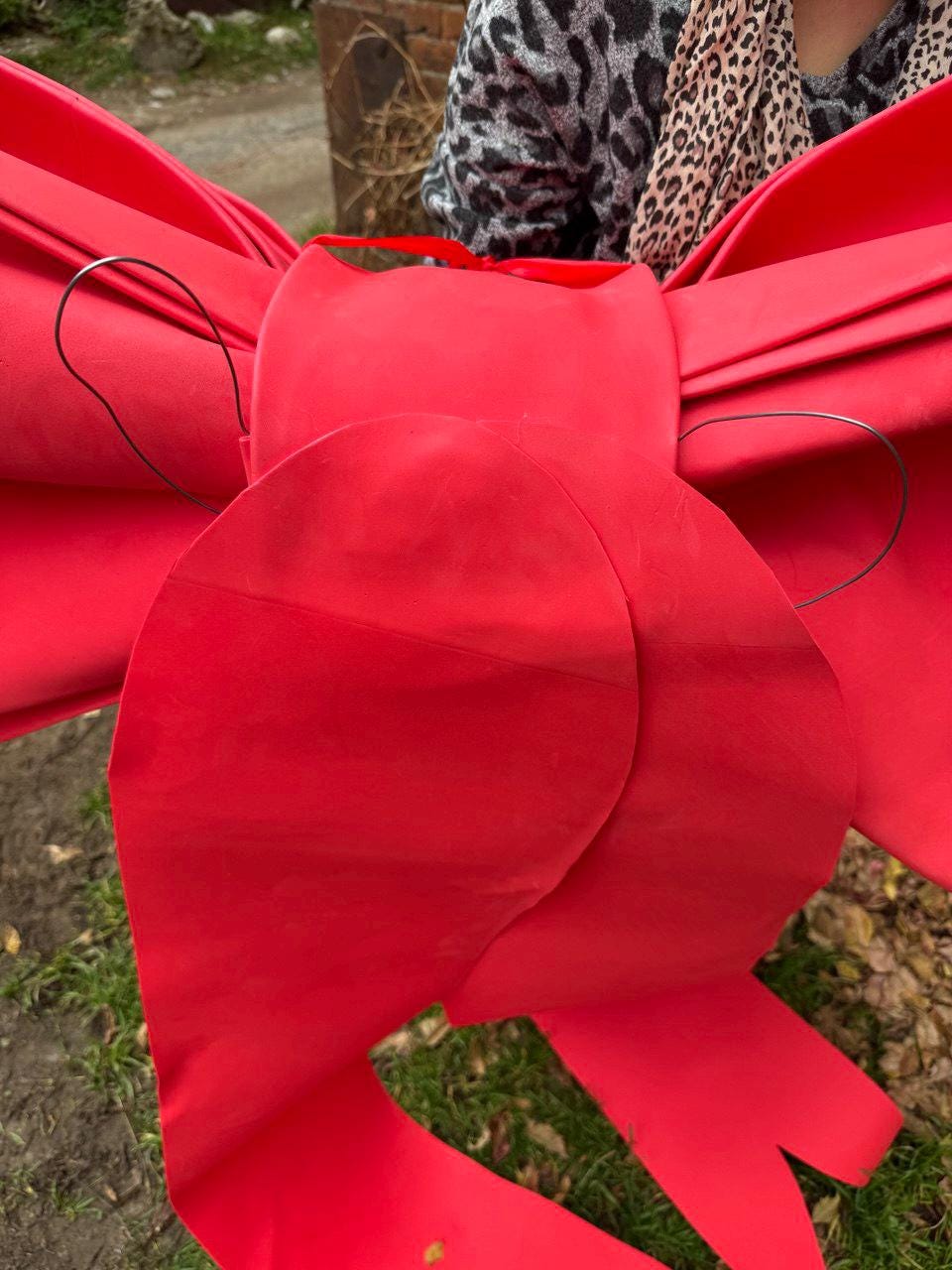 May include: A large, bright red bow made of fabric. The bow has multiple layers and loops, with a wire structure for support. The bow is designed for decoration and is suitable for various festive occasions.