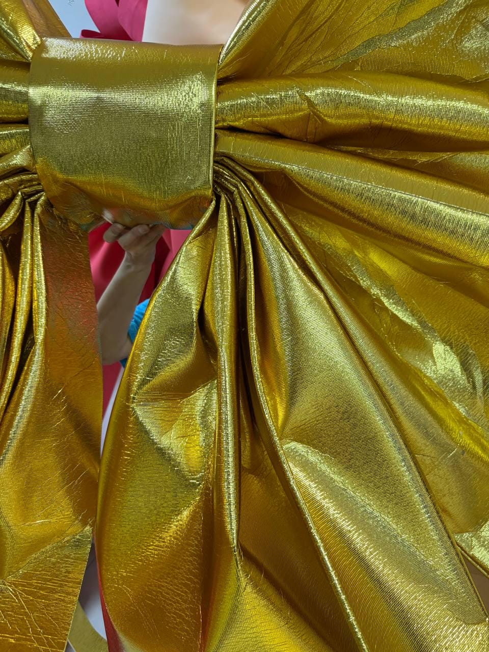 May include: Close-up of a large, gold metallic bow. The bow is made of a shiny, textured material with multiple folds and layers. The bow is a bright, festive gold color, perfect for gift wrapping or decorations.