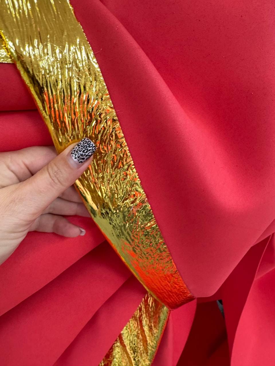 May include: Close-up of red fabric with a gold metallic trim. The fabric is folded, creating a layered effect. The gold trim has a textured, crinkled appearance, adding visual interest to the design.