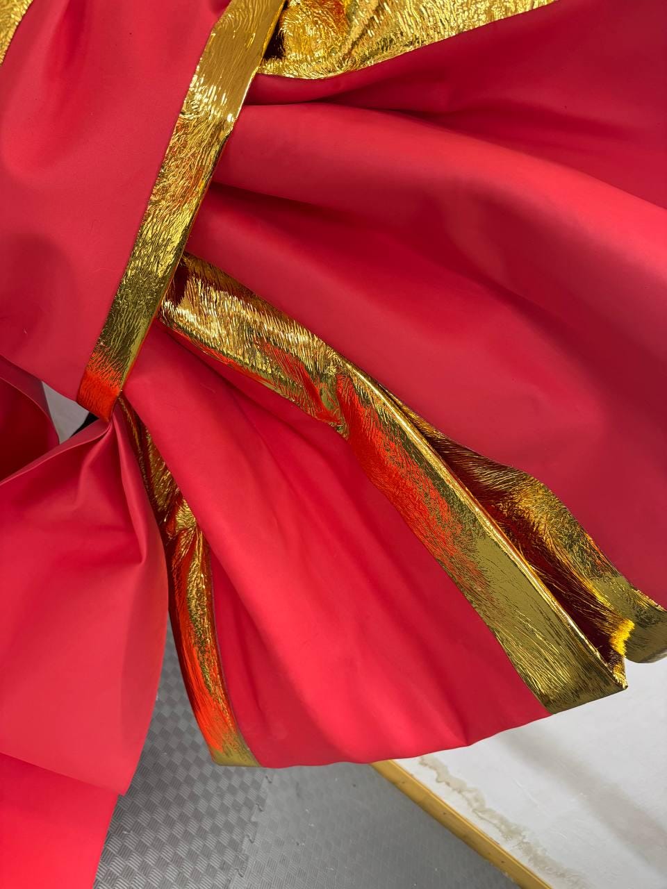 May include: Close-up of vibrant red fabric with gold metallic trim. The fabric is draped and folded, creating a layered effect. The gold trim adds a touch of luxury and contrast to the bold red color.