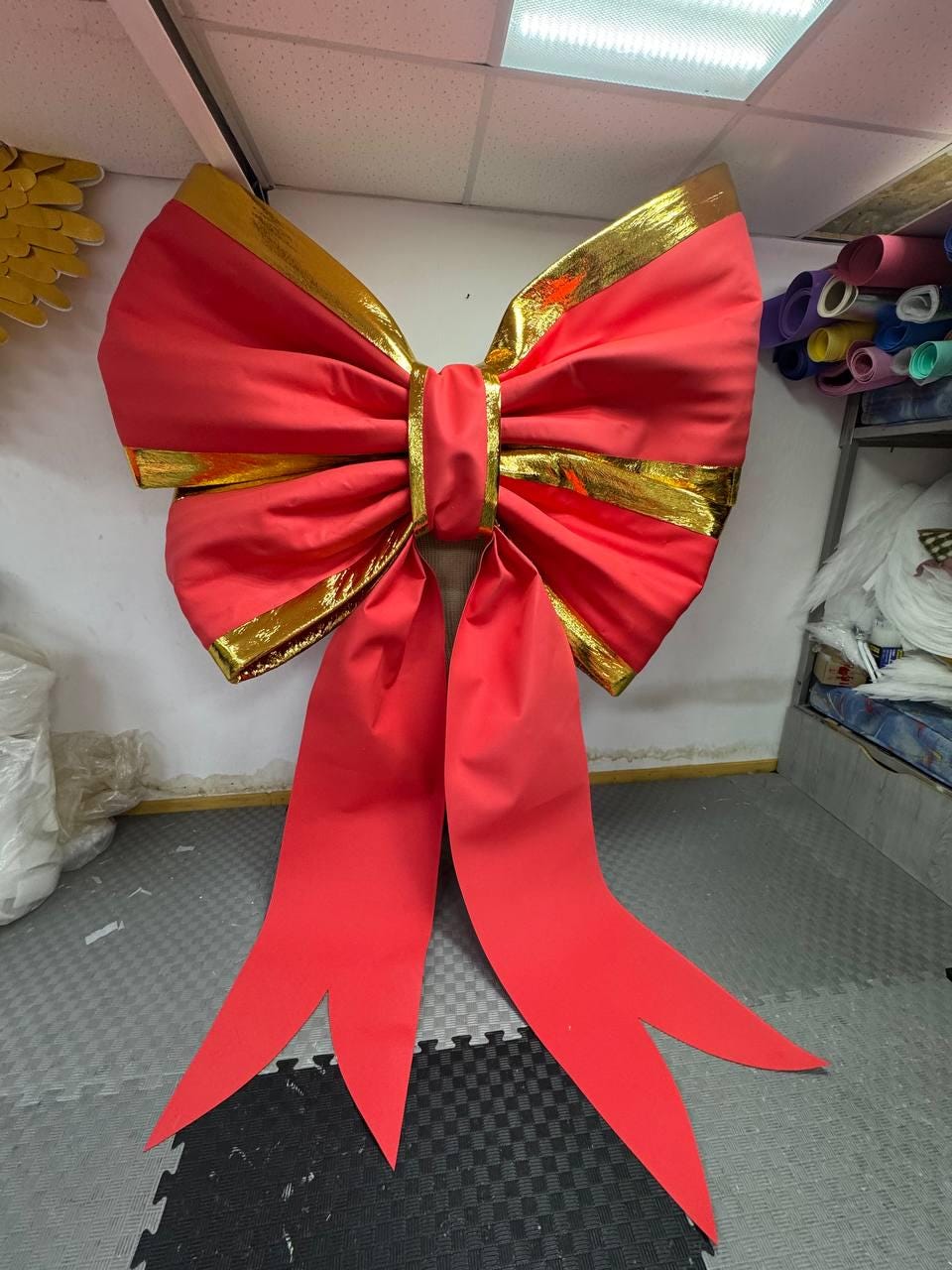 May include: Large, vibrant red bow with gold trim. The bow features a classic design with long, flowing tails. The gold trim accents the edges of the bow, adding a touch of elegance. Perfect for holiday decorations or gift wrapping.