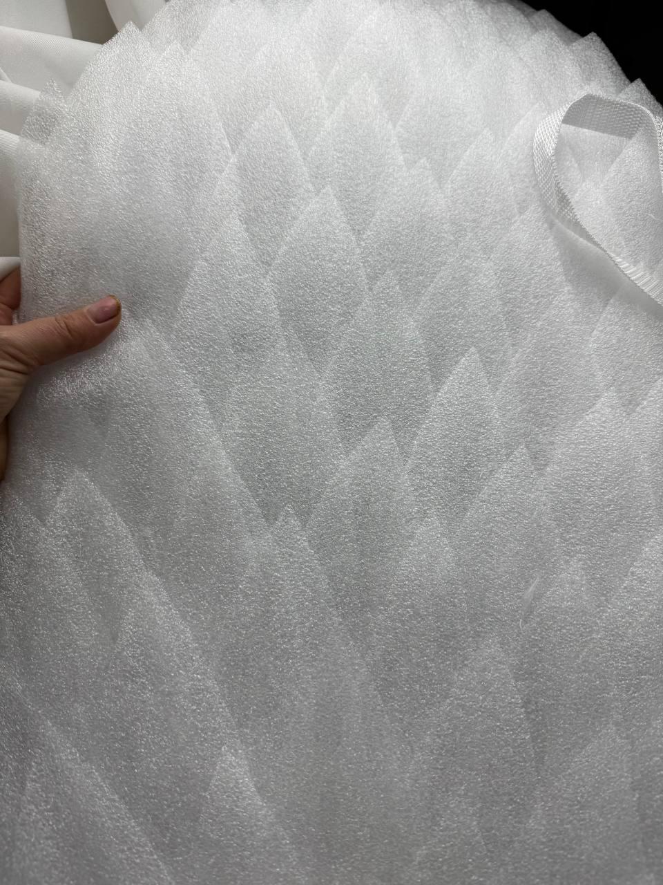 May include: Close-up of a stack of white, diamond-patterned foam sheets. The foam has a textured surface and a soft appearance. A hand is visible on the left side of the image, holding the foam.