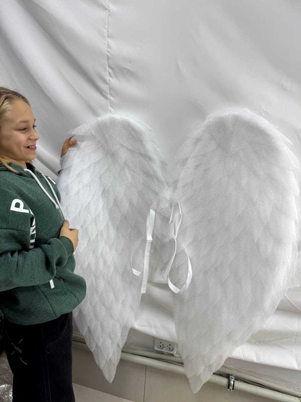 May include: Large, white angel wings with a feathery texture. The wings are made of a soft, lightweight material and are tied together with white ribbons. The wings are displayed against a white backdrop.