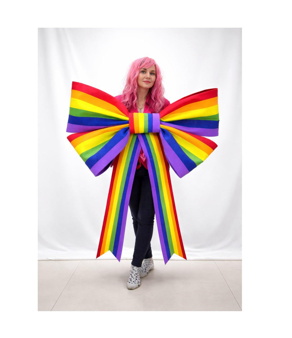 May include: A large, colorful rainbow bow with long streamers. The bow features the colors of the rainbow: red, orange, yellow, green, blue, and purple. The bow is a decorative item, possibly for a party or event.