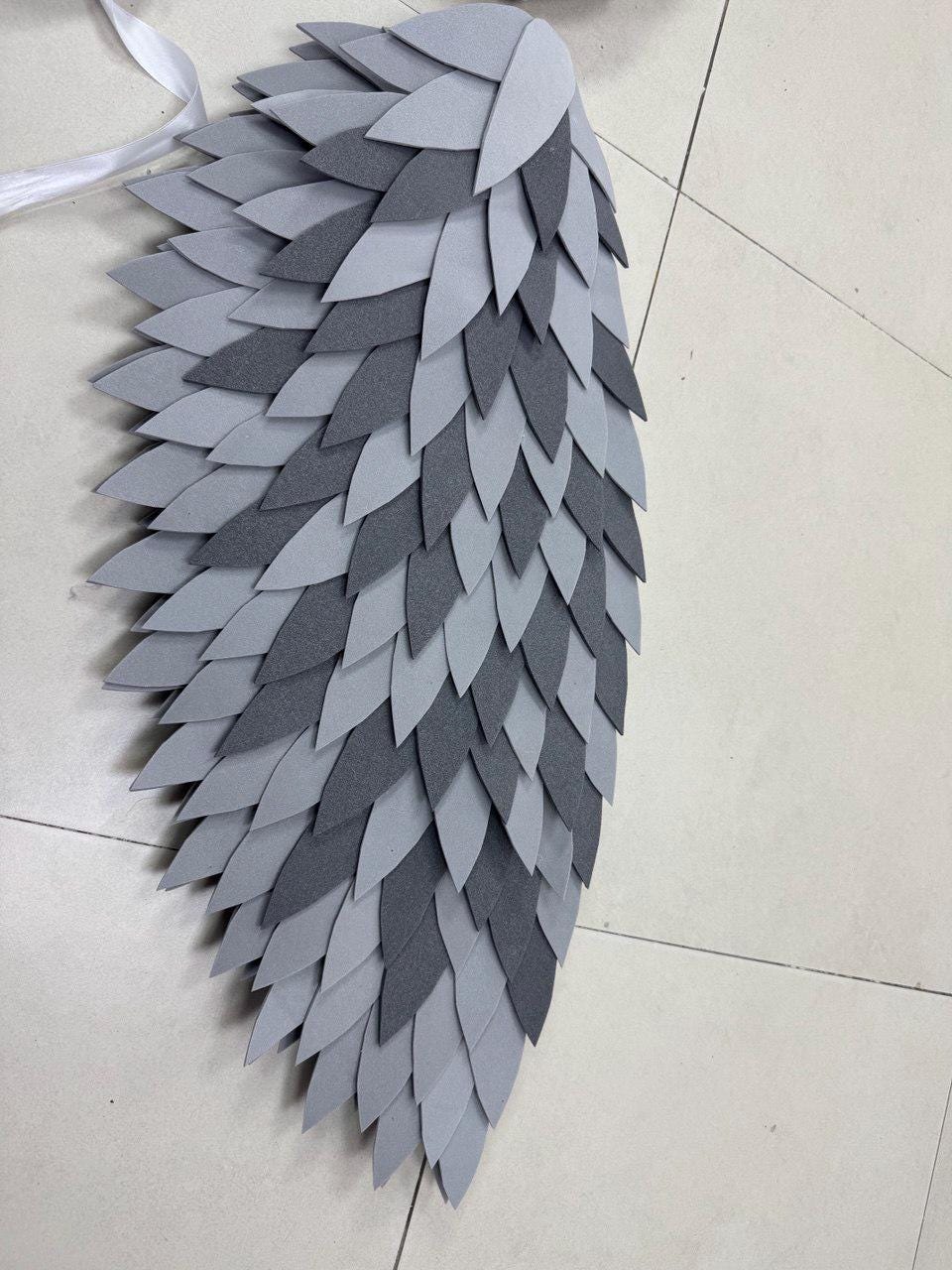 May include: A gray and white layered wing made of felt. The wing is composed of multiple layers of gray and white felt cut into a leaf shape. White ribbon is attached to the top of the wing.