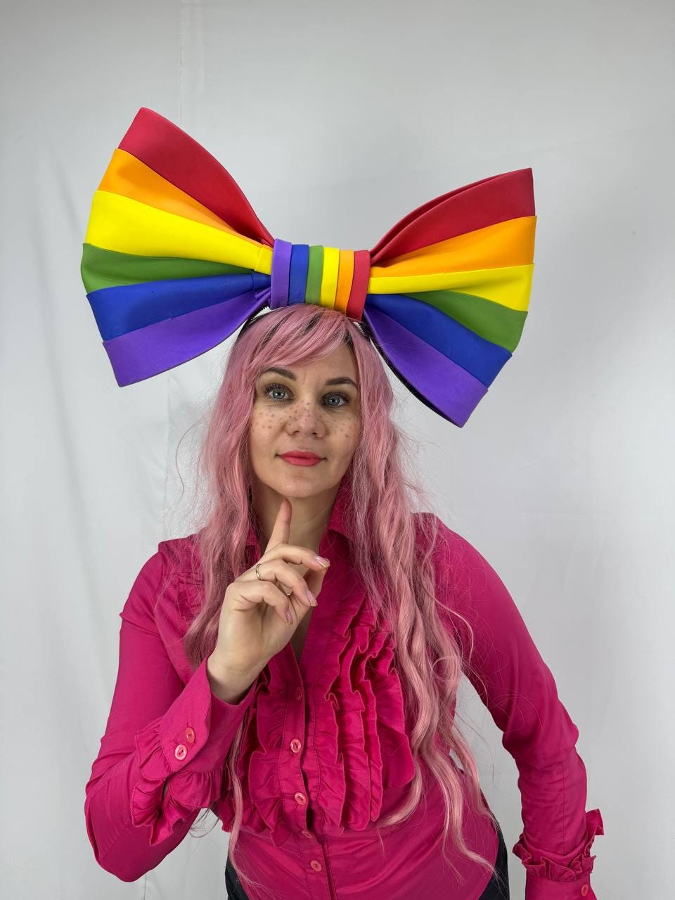 May include: A large rainbow-colored bow headband. The bow features the colors of the rainbow: red, orange, yellow, green, blue, and purple. The headband is a festive accessory, perfect for Pride events or costume parties.