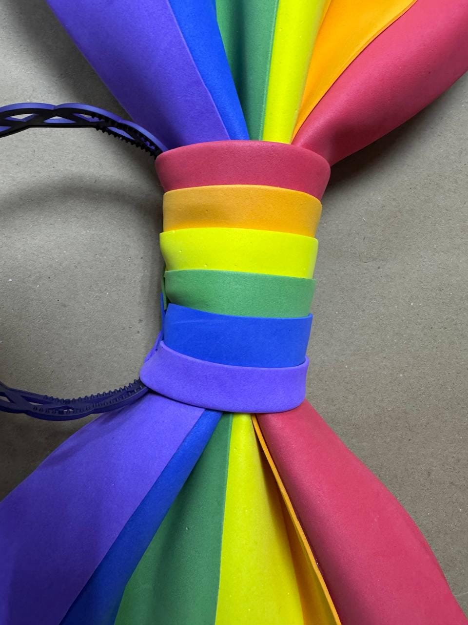 May include: A colorful rainbow-themed headband. The headband features a spectrum of colors, including red, orange, yellow, green, blue, and purple. The colors are arranged in a gradient pattern, creating a vibrant and eye-catching accessory.