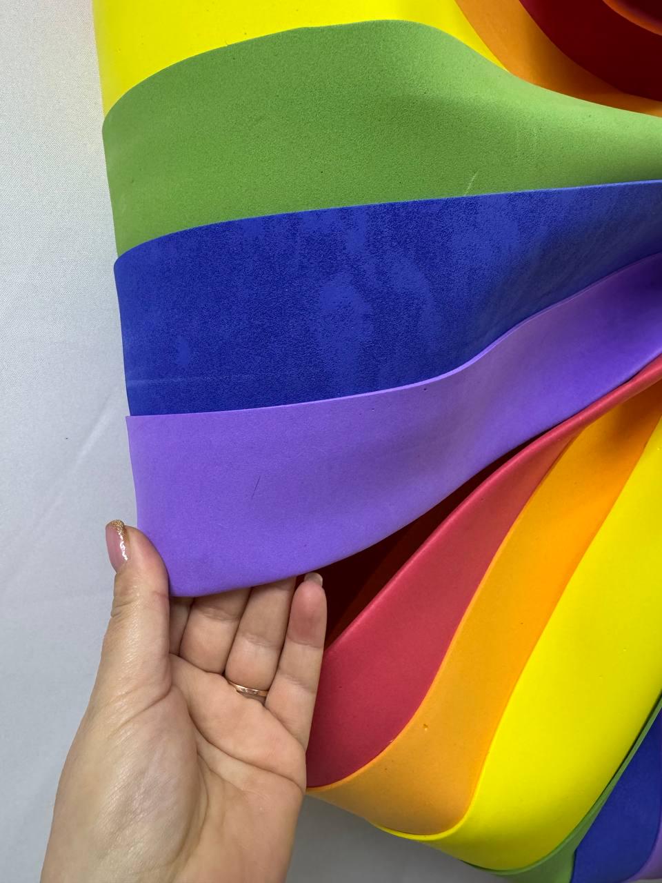 May include: A close-up of a rainbow-colored object with layers of yellow, green, blue, purple, red, and orange. The object is being held by a hand. The colors are vibrant and the layers are curved.