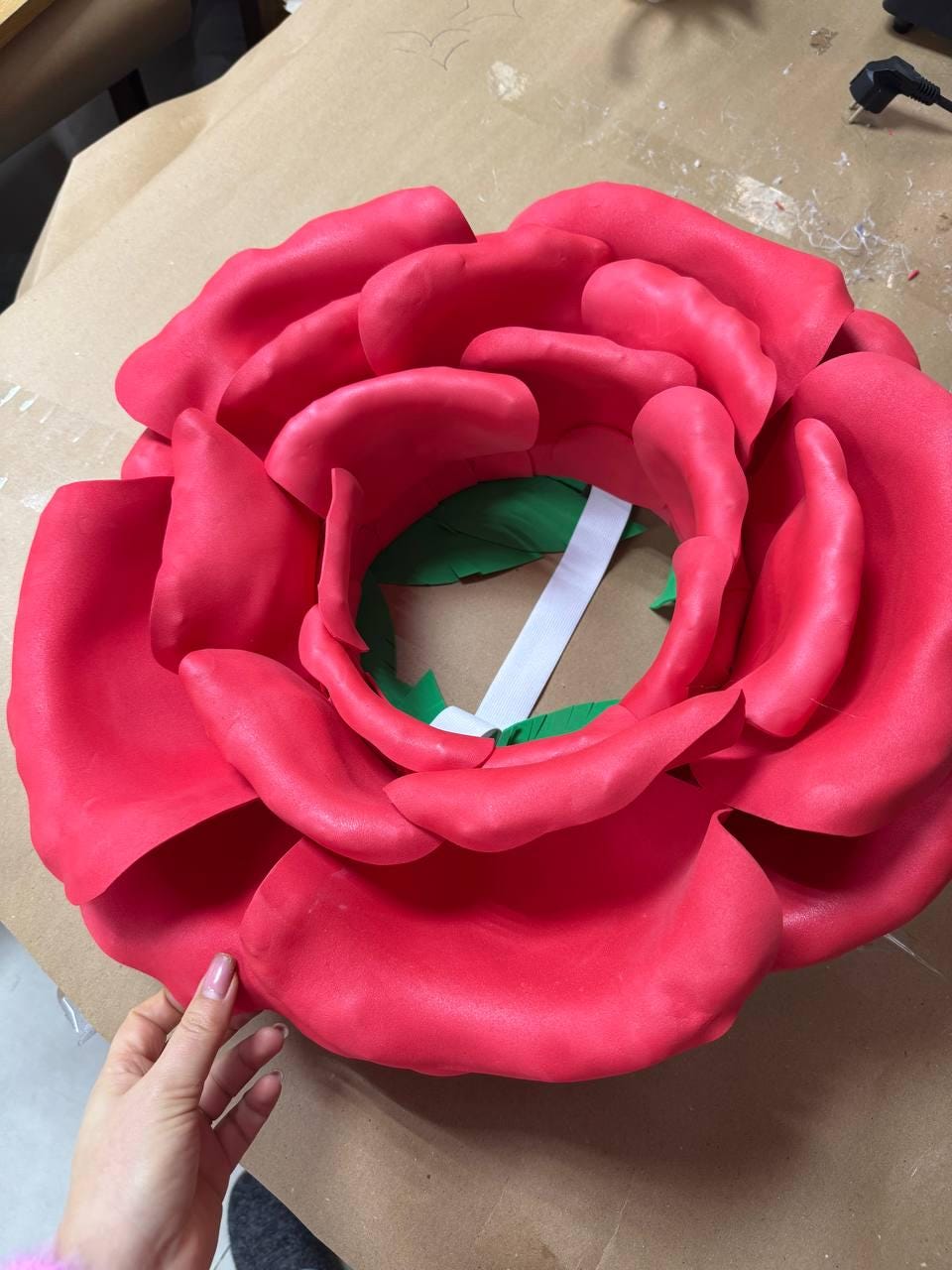 May include: A large, vibrant red rose made of a soft material. The petals are layered and detailed, with a green and white interior. The rose is a decorative item, possibly for a wall or event.