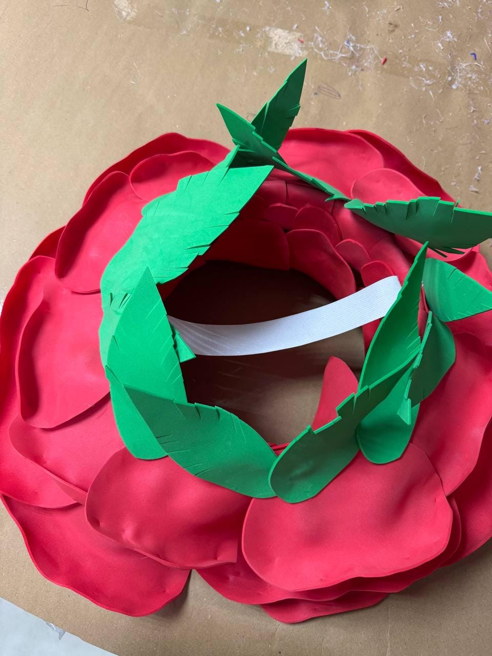 May include: A large, handmade red rose wreath with green leaves. The wreath is made of foam and has a white strip in the center. The petals are layered to create a realistic look. Perfect for home decor or special events.
