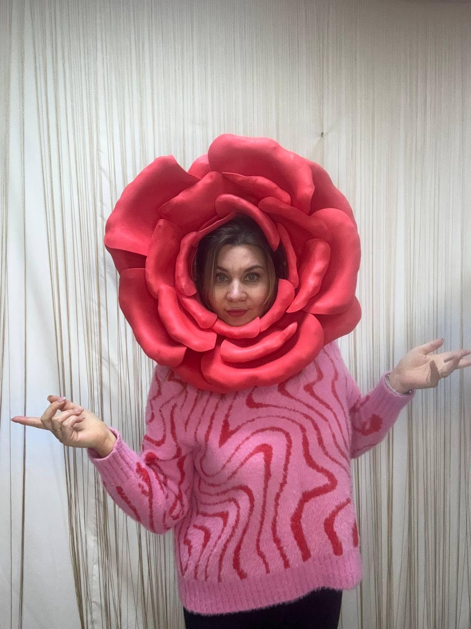 May include: A woman wearing a large, red rose headpiece and a pink sweater with a red, wavy pattern. The rose is a vibrant, eye-catching costume element. The sweater adds a contrasting texture and color.