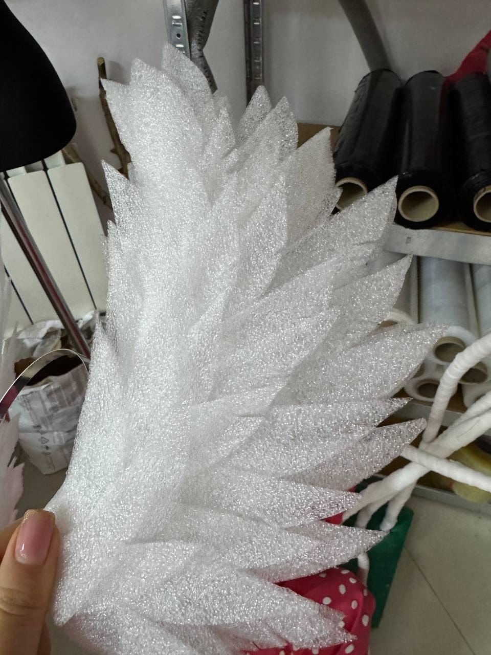 May include: A close-up of a white, feather-shaped object made of a textured foam material. The object has a series of pointed, leaf-like shapes arranged in a layered pattern. The background shows other crafting supplies.
