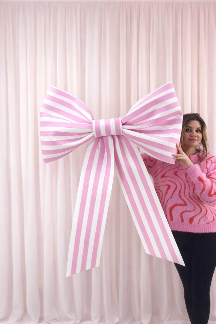 May include: A large, decorative bow with pink and white stripes. The bow is made of a sturdy material and has long, flowing ribbons. The bow is a festive decoration, perfect for parties, weddings, or other special events.