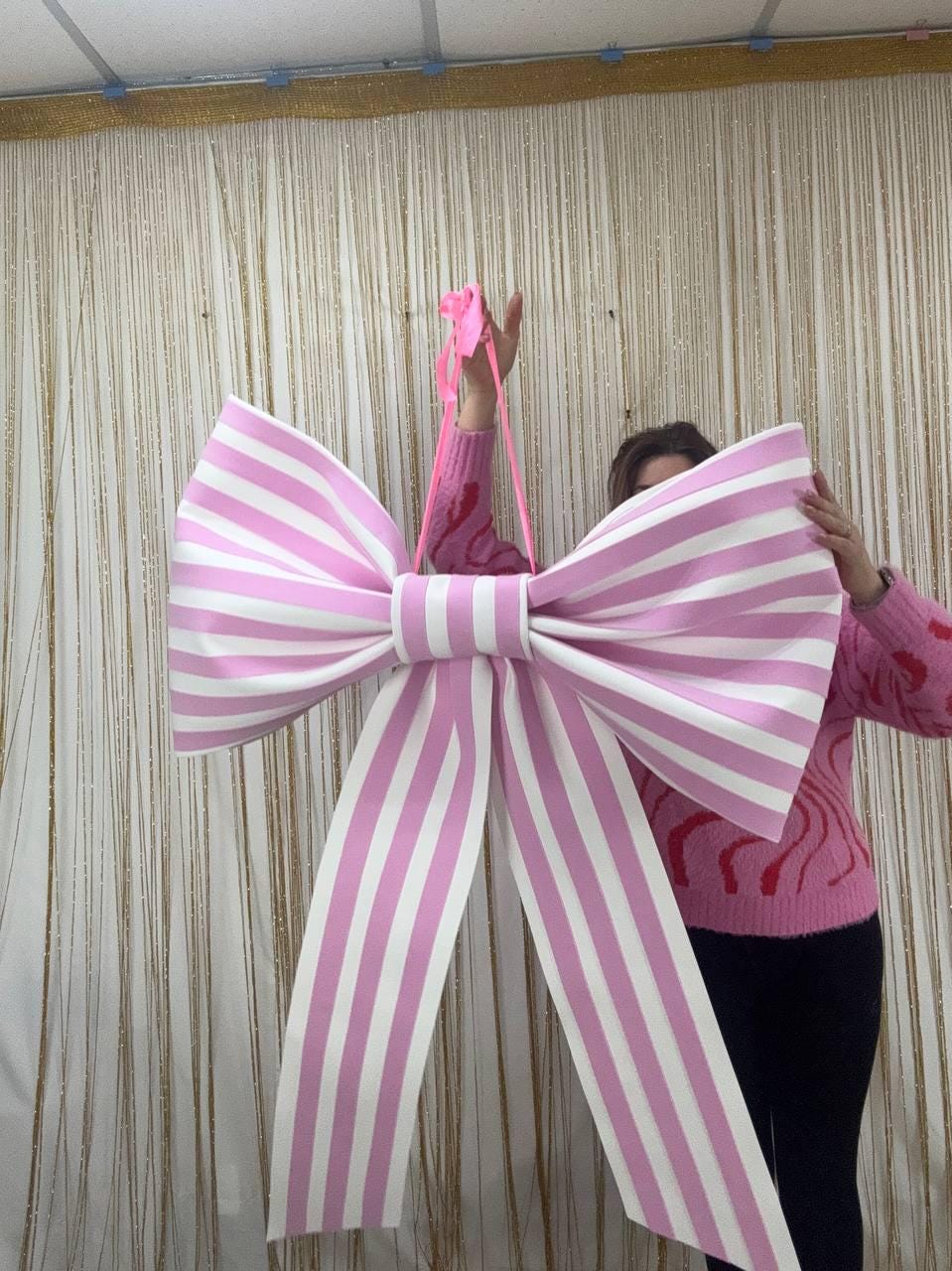 May include: A large, decorative bow with alternating pink and white stripes. The bow is held up by a pink ribbon. The bow is a festive decoration, suitable for parties or events.