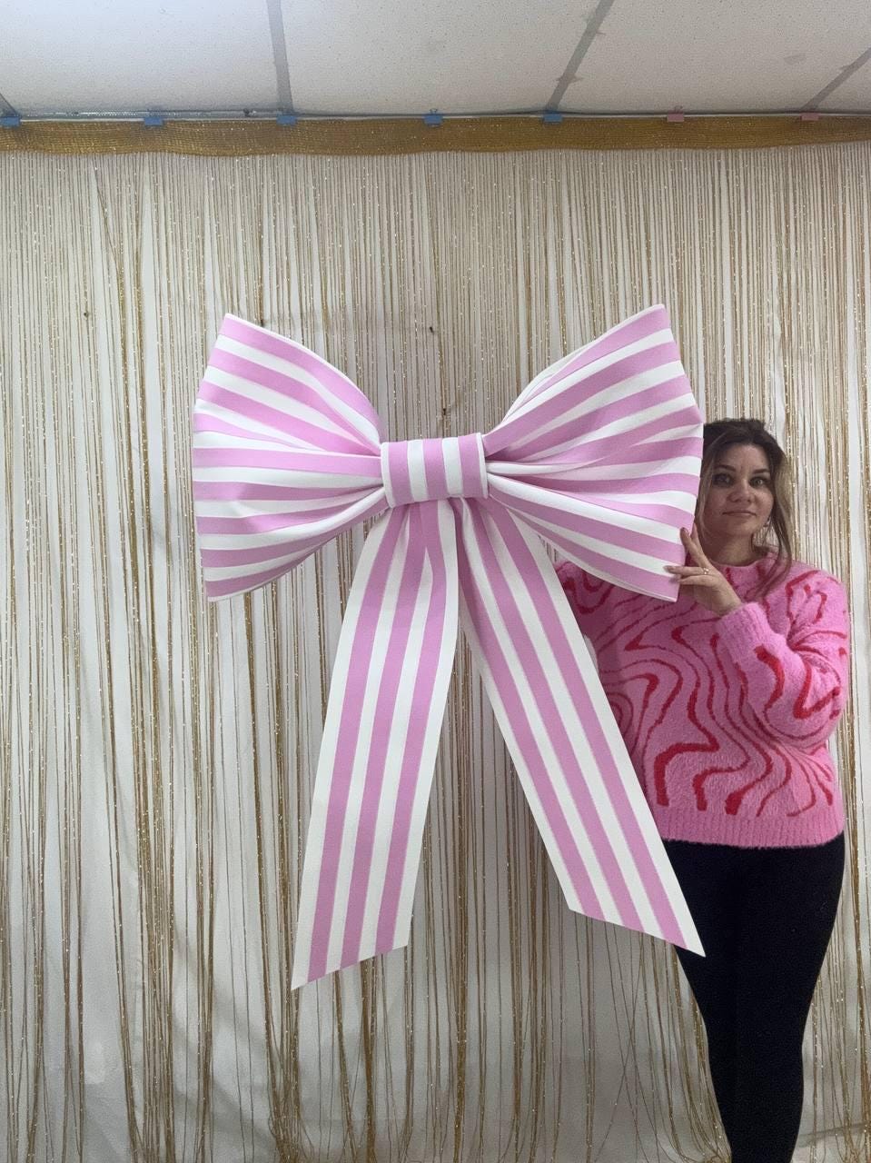 May include: A large, decorative bow with pink and white stripes. The bow is made of a sturdy material and has long, flowing tails. The bow is a festive decoration, suitable for parties, events, or as a unique gift wrapping accent.