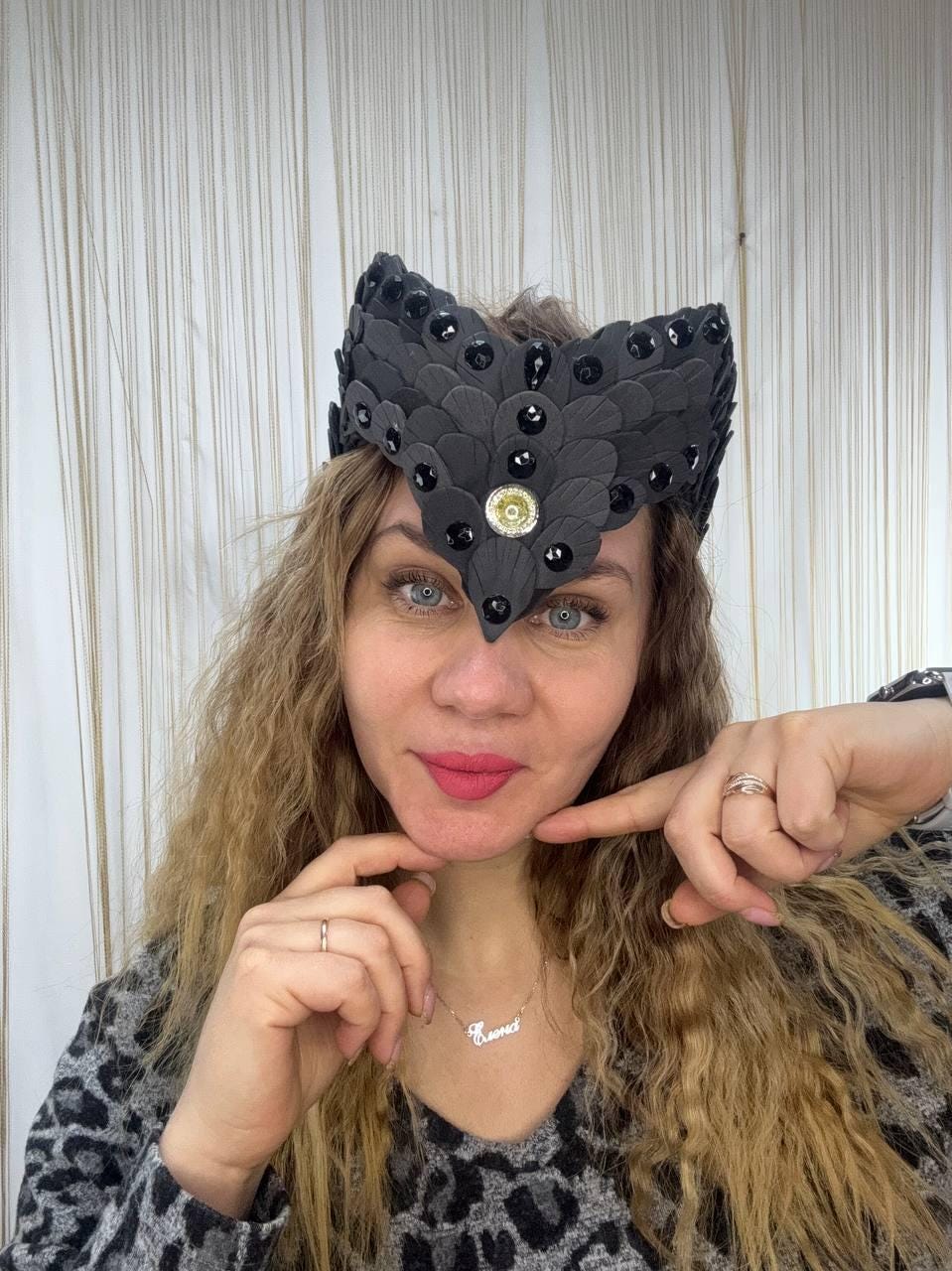 May include: A black, decorative headpiece with a layered, petal-like design. The headpiece is adorned with black gemstones and a central gold-colored embellishment. The accessory is worn on the head.