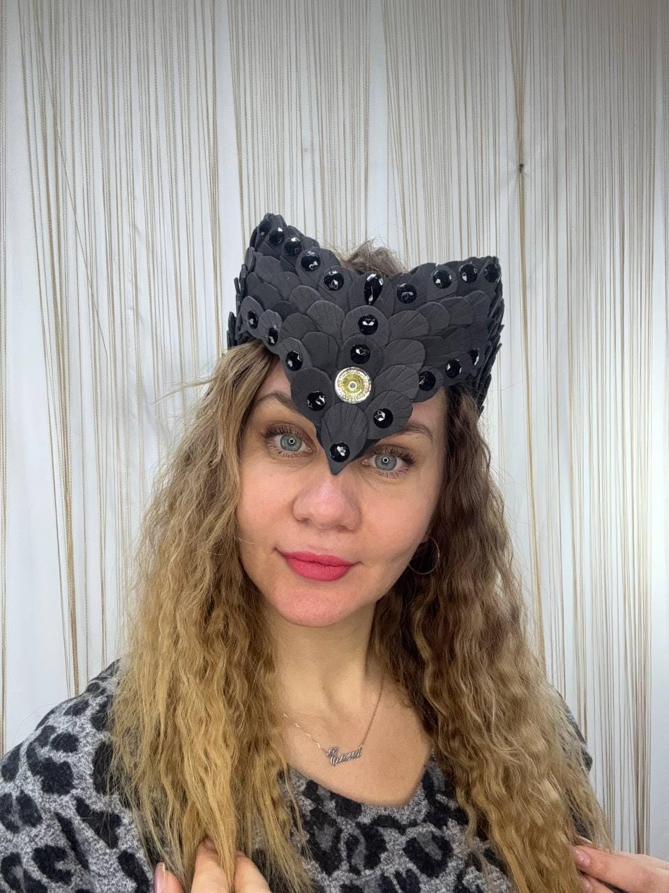 May include: A black headpiece with a layered, feather-like design, adorned with black gemstones and a central gold-toned embellishment. The headpiece is worn on the head.