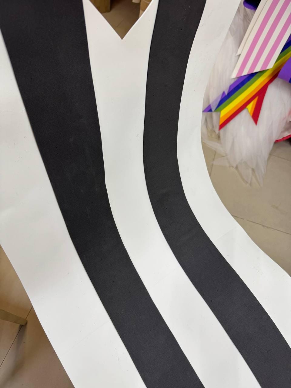 May include: A curved, abstract design featuring alternating black and white vertical stripes. The stripes create a flowing, wave-like pattern. The design is simple and graphic, with a high-contrast color scheme.